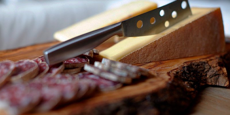 Tabla de madera con salchichón y queso cortado con cuchillo clavado